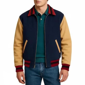 May include: A navy blue and tan varsity jacket with a red and black striped collar and cuffs. The jacket has a zip-up front and two front pockets. The sleeves are tan, and the body is navy blue.