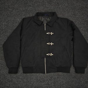 May include: A black jacket with a collar, zip, and three toggle fastenings. The jacket has a ribbed hem and cuffs. The jacket is made of a dark, possibly wool, material.