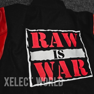 May include: Black jacket with red sleeves featuring a white-bordered patch. The patch displays the words "RAW IS WAR" in red, with a white stripe separating the words. The text "XELEC WORLD" is below the patch.