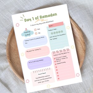 May include: A colorful Ramadan daily planner with pastel-colored boxes and text. The planner includes sections for fasting, goals, and good deeds. The text "Day 1 of Ramadan" is at the top, with the phrase "I start my day with Bismillah!" below it.
