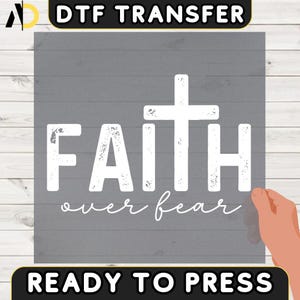 May include: A grey DTF transfer with the words "FAITH over fear" in white, featuring a cross design. The text "READY TO PRESS" is at the bottom. The image is on a grey wooden background.