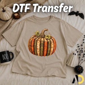 May include: A beige short-sleeve t-shirt featuring a graphic of a pumpkin constructed from vertical vintage book spines in shades of orange, green, and cream. The text DTF Transfer is visible at the top of the image, with a black mug labeled BOO.