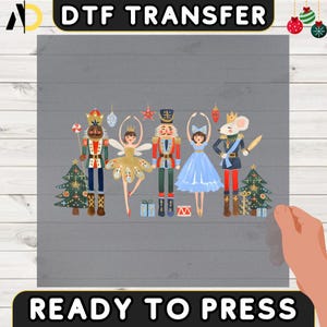 May include: DTF transfer featuring a festive design with characters from The Nutcracker ballet. The design includes a toy soldier, a ballerina, and a mouse king, along with Christmas trees and ornaments. The words "READY TO PRESS" are also visible.