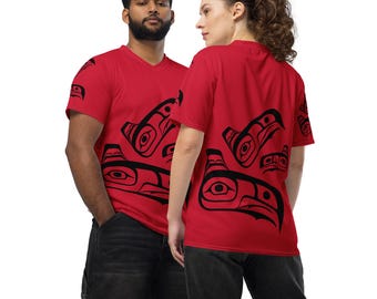 May include: Two people wearing red short-sleeved t-shirts with a black and white graphic print of stylized bird faces. The design is inspired by Indigenous art.