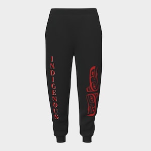 Puede incluir: Pantalones deportivos negros con la palabra "INDIGENOUS" impresa verticalmente en rojo en la pierna izquierda. Un diseño gráfico rojo está impreso en la pierna derecha. Los pantalones deportivos tienen cintura con cordón y puños elásticos.