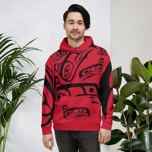 May include: A red hooded sweatshirt with a black and white pattern of stylized animal faces. The pattern is inspired by Indigenous art.