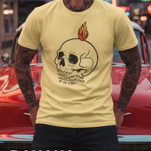May include: A yellow t-shirt with a skull graphic and the text "DON'T COME TOME UNLESS YOUR HAIR IS ON FIRE!". The word "BANANA" is printed at the bottom of the image. The shirt is short-sleeved.