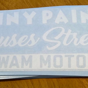 Puede incluir: Una pila de calcomanías de vinilo blanco con el texto "Shiny Paint Causes Stress Wigwam Motors" sobre un fondo azul claro.