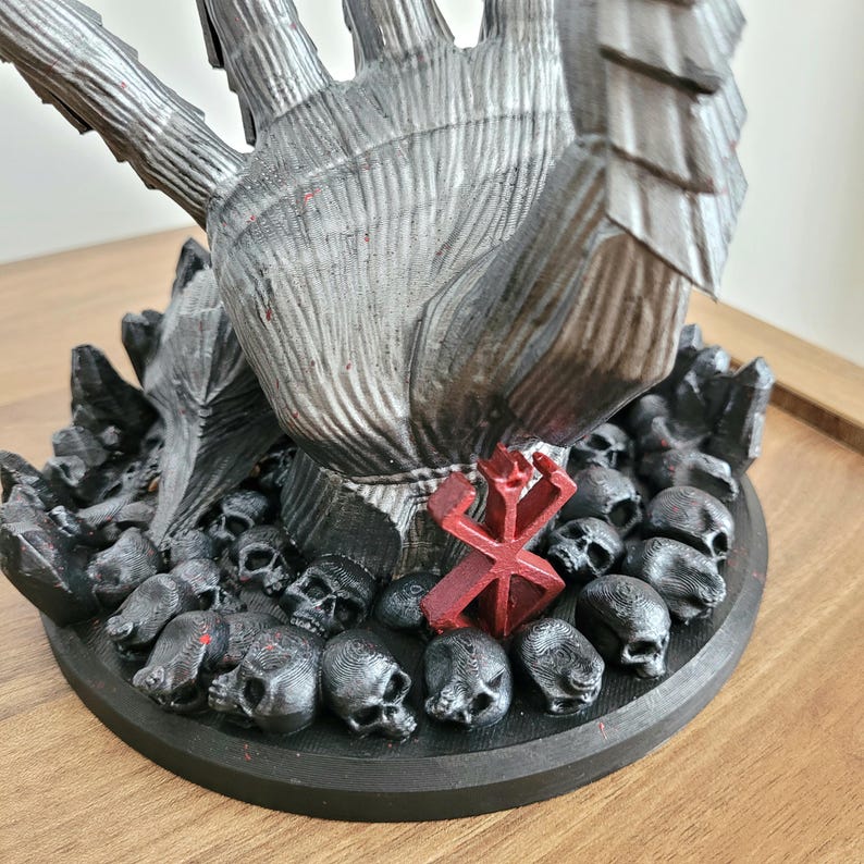May include: A 3D printed sculpture featuring a large, textured grey hand reaching upward from a circular base covered in numerous small black skulls. A prominent red symbol is positioned at the base of the hand, surrounded by the dark, detailed skulls.