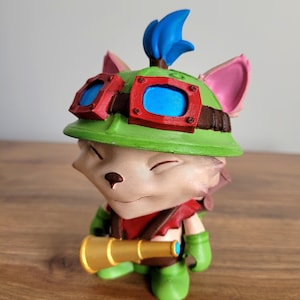 Op de afbeelding: Een 3D-geprint beeldje van een cartoonvos met een groene hoed met een bril, een rode bandana en een gouden telescoop. De vos heeft een knipogende uitdrukking.