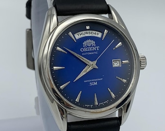 Vintage Orient Automatic herenhorloge met blauwe wijzerplaat, dag- en datumweergave, gemaakt in Japan.