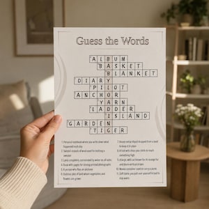 May include: A white paper game sheet titled Guess the Words featuring a crossword puzzle with black text and lines. The grid includes words like Album, Basket, Blanket, Diary, Pilot, Anchor, Yarn, Ladder, Island, Garden, and Tiger with numbered clues.