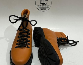 May include: A pair of tan leather hiking boots with black soles and black laces. The boots have a classic design with a high ankle and a sturdy sole. The boots are displayed on a white surface. The logo "LEATHER LORDS" is visible in the background.