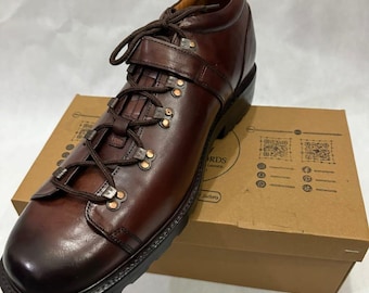 May include: A single brown leather boot with a lace-up design and a buckle strap. The boot has a rounded toe and a thick black sole. The boot is sitting on a brown cardboard box.