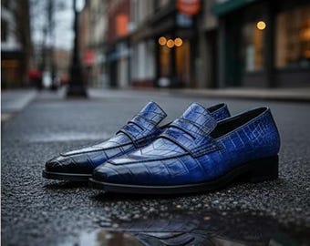 May include: A pair of blue leather loafers with a crocodile skin texture. The shoes are displayed on a wet, asphalt surface, reflecting the city street background. The loafers have a classic design with a low heel.