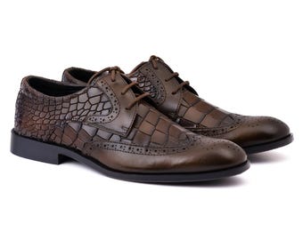 Puede incluir: Un par de zapatos oxford de cuero marrón oscuro con un patrón texturizado de piel de cocodrilo en los paneles laterales y una puntera lisa con perforaciones decorativas tipo brogue. Incluyen cordones marrones y suela negra.