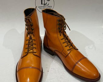 May include: A pair of orange leather boots with a glossy finish. The boots have a cap toe design, brown laces, and a dark brown sole. The boots are from Leather Lords.
