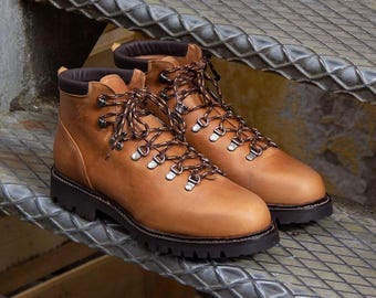 May include: A pair of brown leather hiking boots with dark brown laces and metal eyelets. The boots have a black sole and a padded collar. The boots are sitting on a metal surface.