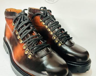 May include: A pair of brown and black leather boots with black laces and brass eyelets. The boots have a thick black sole and a gradient color effect from brown to black. The boots are likely handcrafted.