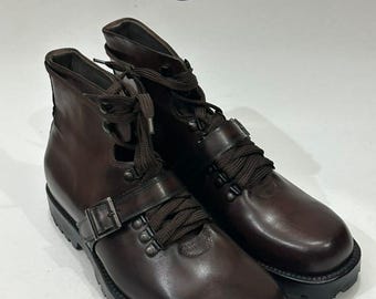 May include: A pair of brown leather boots with a buckle closure and dark brown laces. The boots have a rugged sole and a high-top design. The image includes the text "LEATHER LORDS" in a circular logo.