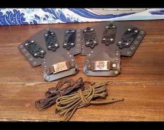 May include: Two brown leather wrist guards with metal accents and a decorative design. The guards are on a wooden surface with two cords, one brown and one gold.