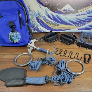 May include: A collection of tactical equipment, including a blue backpack, grappling hook, and climbing rings. Black leather claw-like devices and ropes are also present, arranged on a wooden surface.