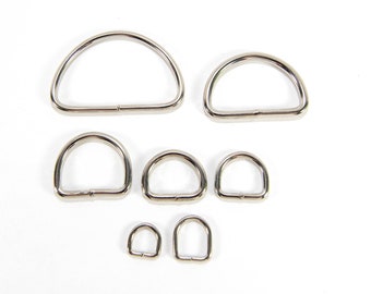 May include: A set of seven silver metal D-rings of varying sizes. The rings are arranged in a staggered pattern on a white background.