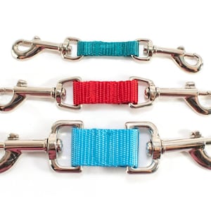 May include: Three double-ended metal swivel snap hooks connected by short, flat nylon webbing straps in teal, red, and bright blue. Each connector features a polished silver-tone finish with spring-loaded clips on both ends for secure attachment.