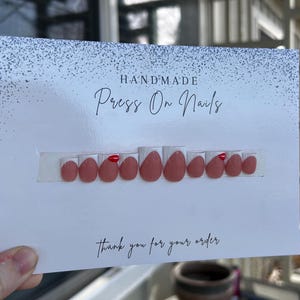 K&ouml;nnte beinhalten: Ein Set handgefertigter Press-On-N&auml;gel in einem ged&auml;mpften Rosaton mit gl&auml;nzendem Finish. Die N&auml;gel sind auf einer wei&szlig;en Karte mit den Worten "HANDMADE Press On Nails" und "thank you for your order" angeordnet.