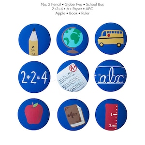 Peut inclure: Neuf boutons ronds bleus avec différentes images sur le thème de l'école. Les boutons représentent un crayon, un globe terrestre, un bus scolaire, une équation mathématique, un papier avec une note A+, de l'écriture cursive, une pomme, un livre et une règle.