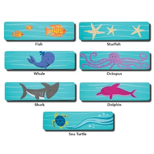 May include: A set of six colorful wooden tiles featuring different sea creatures, including a fish, starfish, whale, octopus, shark, and sea turtle. Each tile has a blue background with white waves and the name of the creature printed below the image.