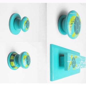 May include: Set of three turquoise blue cabinet knobs with a green and yellow sea turtle design. The knobs are made of wood and have a round shape. The larger knob is a pull handle with a wave design.