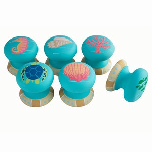Peut inclure: Ensemble de six boutons de cabinet bleu turquoise avec une variété de motifs marins, dont un hippocampe, une coquille, un corail, une tortue et des algues. Chaque bouton a une base dorée et blanche.