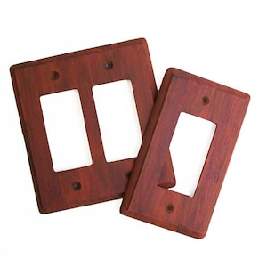 May include: Two wooden wall plate covers, one with two openings and one with a single opening. The covers are a rich reddish-brown color.