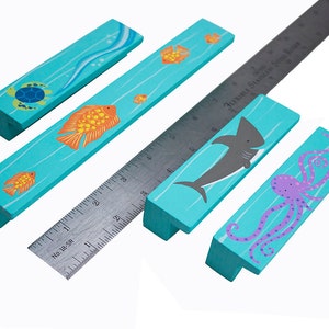 May include: Five turquoise blue wooden drawer pulls with ocean-themed designs. The pulls feature a turtle, a shark, an octopus, and two different fish. The pulls are approximately 4 inches long.
