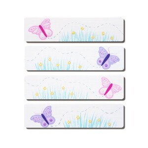 May include: Four rectangular white banners with a blue and green grass design and a butterfly flying over the grass. The butterflies are pink, purple, and light blue.
