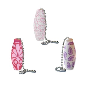 Op de afbeelding: Drie decoratieve ventilator trekkoorden met witte achtergronden en roze, paarse en rode bloemmotieven.