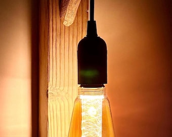 May include: A rustic wall sconce featuring a large Edison-style light bulb. The bulb is suspended from a black cord and mounted on a wooden plank. The light is warm and inviting, perfect for a cozy space.