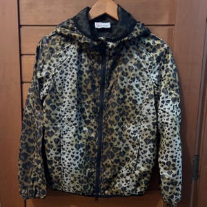 Könnte beinhalten: Kapuzenjacke mit Leopardenmuster in Braun- und Schwarztönen. Die Jacke hat einen durchgehenden Reißverschluss und eine mit Mesh gefütterte Kapuze. Das Valentino-Logo ist am Kragen sichtbar.