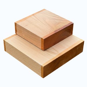 Könnte beinhalten: Zwei quadratische Holzboxen, eine auf der anderen gestapelt. Die Boxen haben eine natürliche Holzmaserung mit helleren Oberflächen und dunkleren Kanten. Die Kanten sind rotbraun.