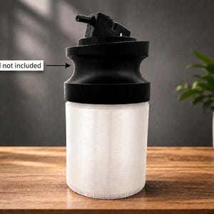 May include: A cylindrical container with a translucent white body and a black top featuring a small nozzle. A text label with an arrow pointing to the black top reads Lid not included. The container has a smooth, matte finish and a simple design.