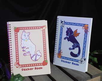 May include: Two spiral bound sticker books with colorful covers. The left book has a white cat with purple stripes on a pink background with strawberries. The right book has a black cat with wings on a blue background with flames. Both books say "Sticker Book" on the cover.