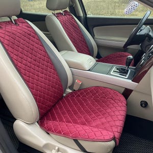 May include: Burgundy car seat covers with a diamond quilted pattern. The covers are installed in a car with tan leather seats and a gray and tan interior. The covers are designed to protect the seats and add a touch of style.