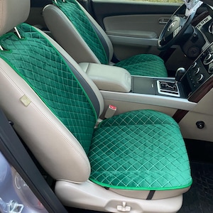 May include: Emerald green car seat covers with a diamond-quilted pattern. The covers have a contrasting green trim and are installed on beige car seats. The interior of the car is visible, including the steering wheel and center console.