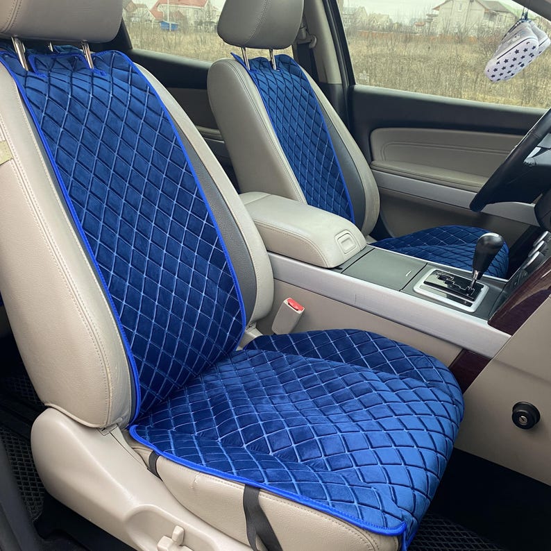 May include: Blue car seat covers with a diamond-quilted pattern. The covers are a deep blue color with a lighter blue trim. The seats are installed in a car with light gray leather seats. The car's interior is visible in the background.