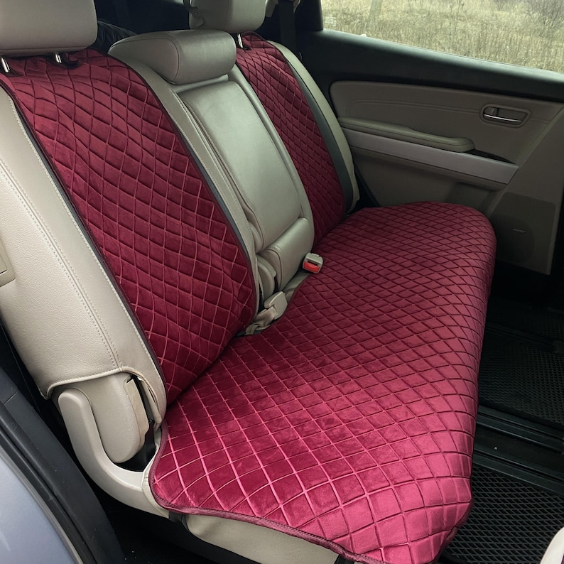May include: Burgundy quilted car seat covers. The covers feature a diamond pattern and are designed to fit the back seat of a vehicle. The covers are made of a soft, plush material and are designed to protect the original seats.