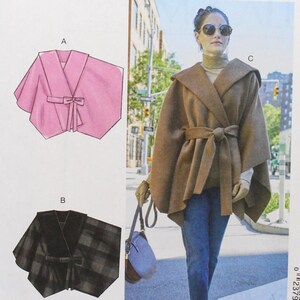 May include: McCall's sewing pattern M8029. The pattern features a pink cape with a tie, a black plaid cape with a tie, and a brown hooded cape with a tie. The size is Y (XSM-SML-MED).