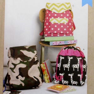 May include: Kwik Sew pattern #K4333 for making three different backpacks. The pattern shows a pink and white polka dot backpack with a yellow and white chevron flap, a camouflage backpack, and a black backpack with a white giraffe print.