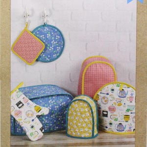 May include: A Kwik Sew pattern for kitchen appliance covers. The image shows a variety of covers, including pot holders, oven mitts, and covers for appliances. The covers feature floral, geometric, and patterned designs in pink, blue, and yellow.