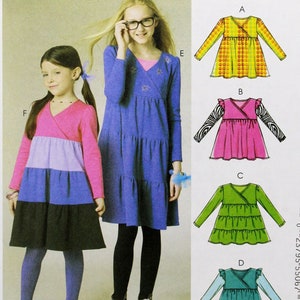 May include: Sewing pattern for a girls' dress with a wrap style bodice and tiered skirt. The pattern includes four different variations of the dress, each with a different color and sleeve style. The pattern is for sizes 3-4-5-6. The pattern is from McCall's and has the number M6157.